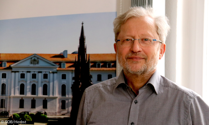 Ein Mann mit Brille und weißen Haaren lächelt in die Kamera