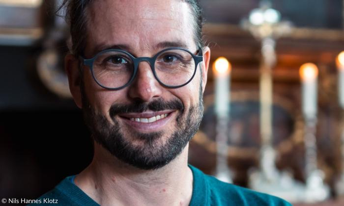 Ein Mann mit runder Brille lächelt in die Kamera