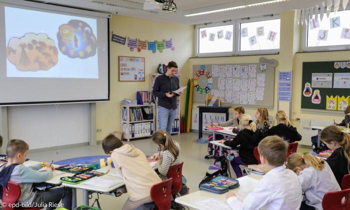 Ein Klassenzimmer, in dem sehr junge Schülerinnen und Schüler sitzen, vorne steht ein Lehrer