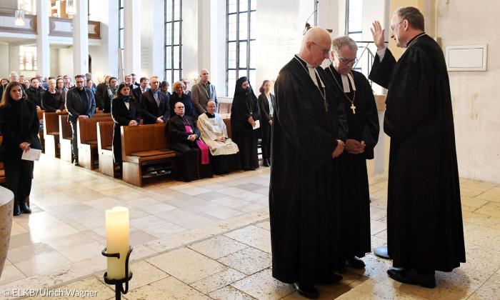 Ein Mann im Talar segnet zwei andere Männer im Talar