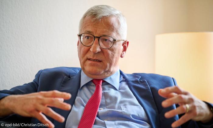 Ein Mann mit Brille und roter Krawatte spricht gestikulierend