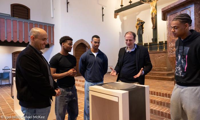 Fünf Männer stehen in einer Kirche um das Taufbecken herum