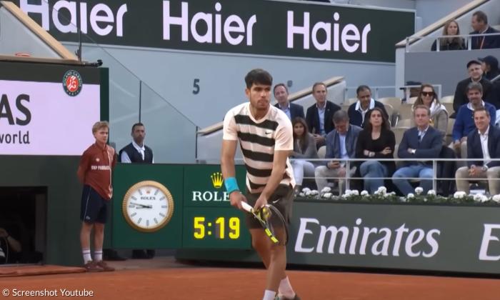 Ein Tennisspieler hat einen Schläger in der Hand, hinter ihm ein Balljunge