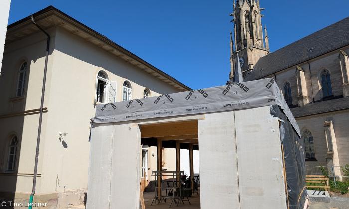 Außenansicht der Baustelle mit der katholischen Herz-Jesu-Kirche im Hintergrund. 