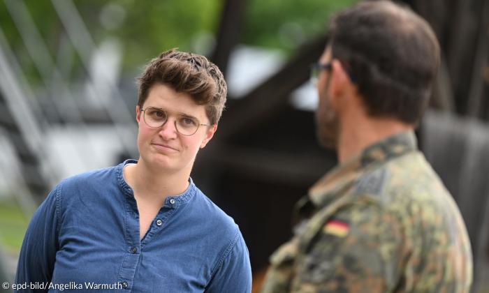 Eine Frau mit Brille, im Vordergrund leicht verschwommen ein Soldat