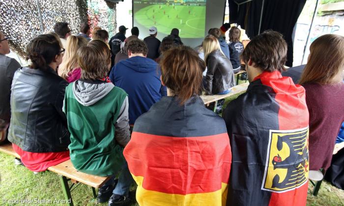 Menschen mit Fahnen schauen Fußball auf einer Leinwand
