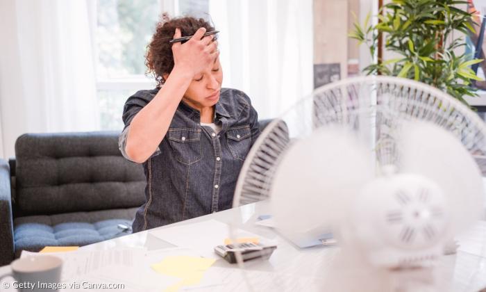 Eine Frau sitzt am Schreibtisch, vor ihr ein Ventilator
