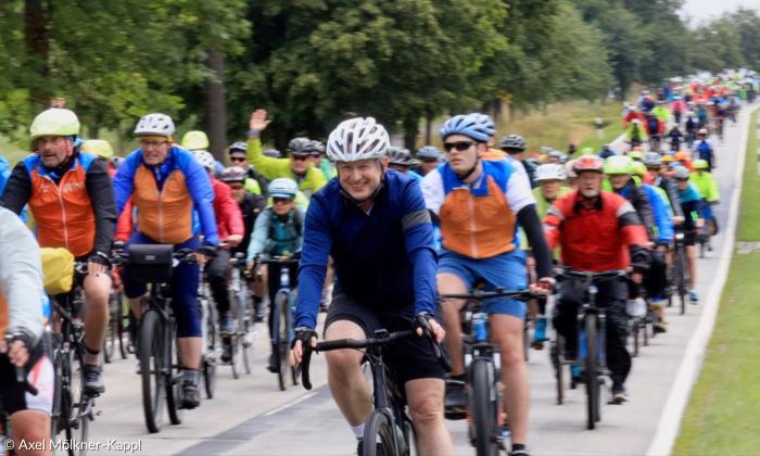 Eine Gruppe von Radfahrer:innen auf einer Straße, alle mit Helm