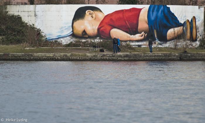 Graffiti an einer 120 Quadratmeter großen Wand in Frankfurt: Der dreijährige Aylan Kurdi liegt tot bäuchlings am Strand, bekleidet mit rotem T-Shirt, blauer Hose und Schuhen.