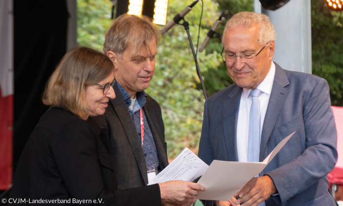 Innenminister Joachim Herrmann überreicht eine Urkunde an Carola Welker (Vorsitzend CVJM Bayern) und an Michael Götz (Generalsekretär CVJM Bayern).