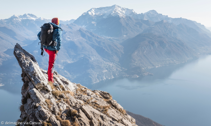 Eine Wanderin steht am Gipfel an einer Klippe und schaut in die Ferne.