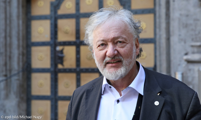Reinhard Bauer, graue Haare und Bart, vor einer alten Tür mit Sacko