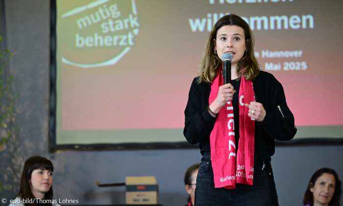 Luisa Neubauer auf dem Podum beim Evangelischen Kirchentag in Hannover mit dem Kirchentagsschal um den Hals und Mikrophon in der Hand