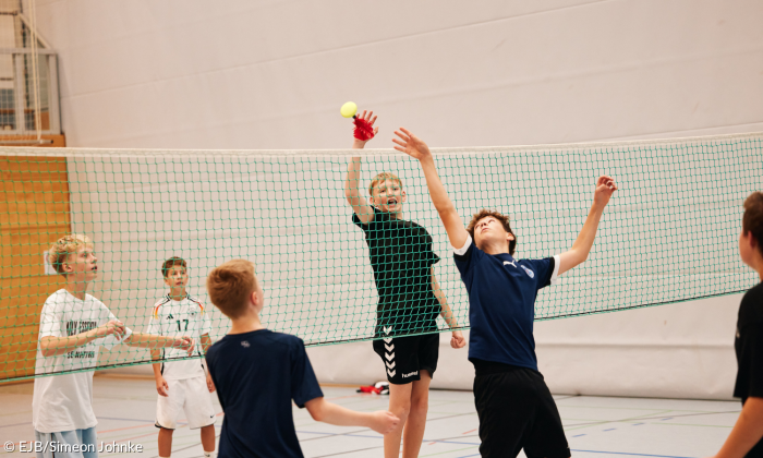 Jugendliche spielen Handfederball in der Turnhalle. Sie springen, schlagen den Ball über das Netz