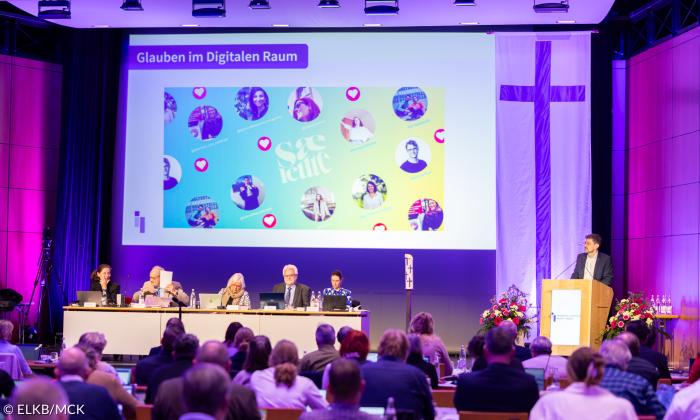 Menschen sitzen in einem großen Raum mit Podium