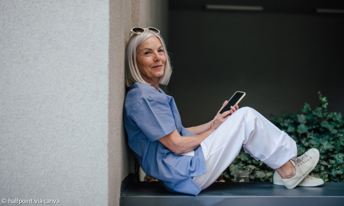 Alte Frau sitzt auf Mauer mit Handy in der Hand