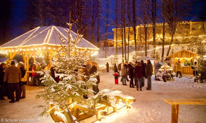 Ein Weihnachtsmarkt im Wald mit Schnee, Buden, Lichter und Menschen. 