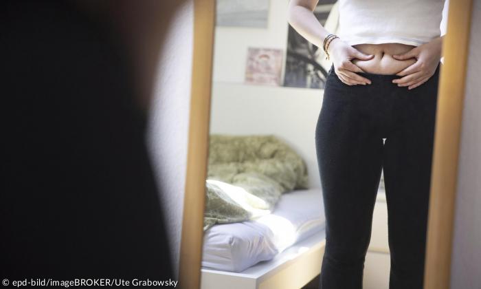 Eine junge Frau überprüft ihren Bauch im Spiegel