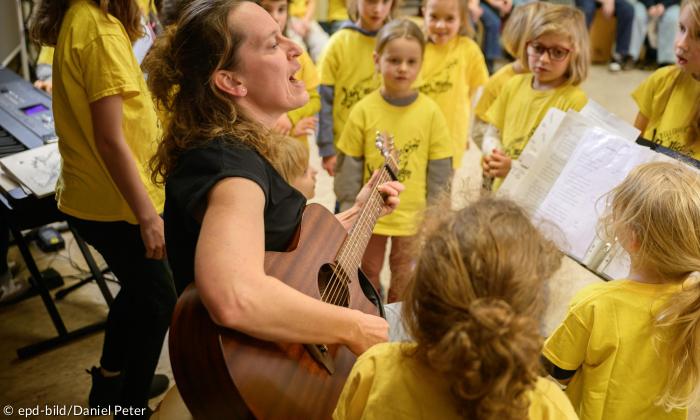 Madlen Schuh spielt auf der Gitarre, drum herum Kinder mit gelben T-Shirts