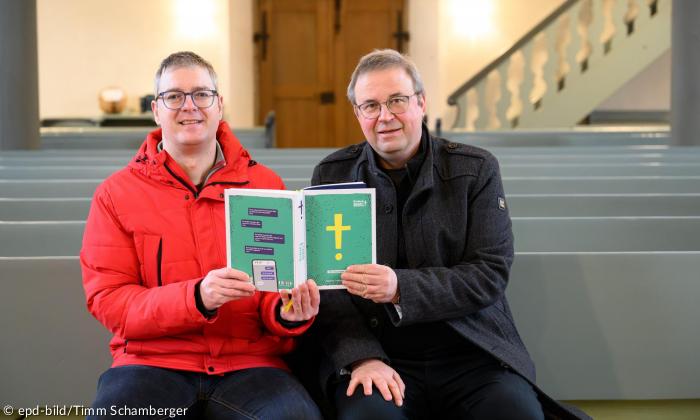 Der liturgische Lektor Elmar Glöckner und Pfarrer Andreas Funk in der Sankt Georgskirche in Möttingen halten gemeinsam das Buch hoch"Einfach Bibel".