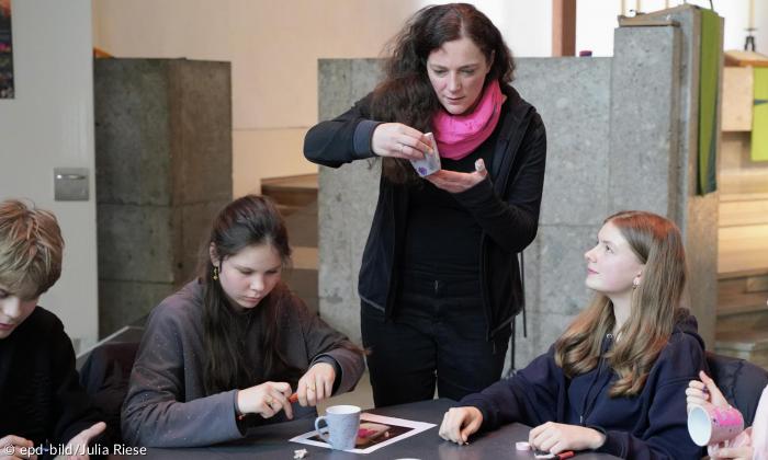 Eine Frau steht, Kinder sitzen an einem Tisch