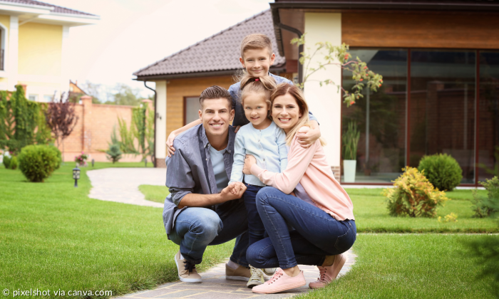 Familie im Garten ihres Hauses schaut in die Kamera. Vater, Mutter und zwei Kinder