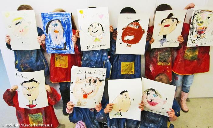 Kinder halten Bilder von Gesichtern vor ihr Gesicht