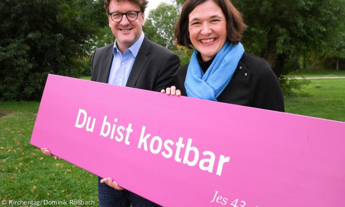 Zwie Menschen halten ein pinkes Schild, auf dem "Du bist kostbar" steht