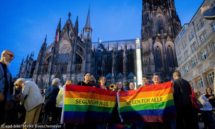 Bunte Fahne mit "Segen für alle" drauf vor einer Kirche