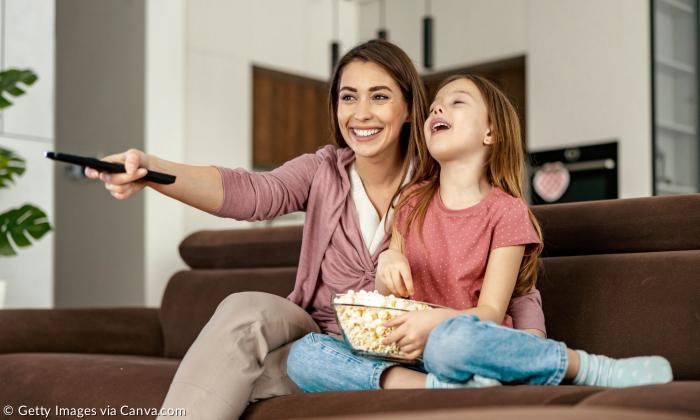 Eine Frau und ein Mädchen sitzen mit einer Schüssel Popcorn auf der Couch
