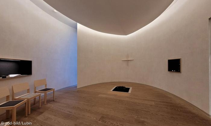 Ein halbrunder Raum mit Stühlen und einem Kreuz an der Wand