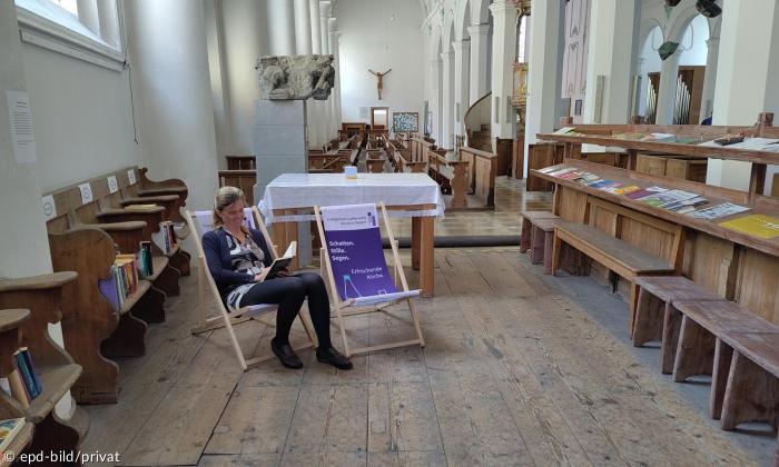 Eine Frau sitzt in einem von zwei Liegestühlen, die in einer Kirche stehen, und liest
