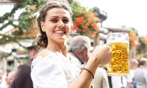 Eine Frau im Dirndl hält einen Maßkrug und grinst