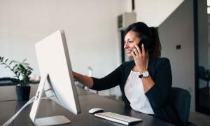 Eine Frau sitzt am Computer, während sie telefoniert.