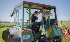 Eine Frau und ein Mann sitzen auf einem Traktor und schauen auf einen Controller.