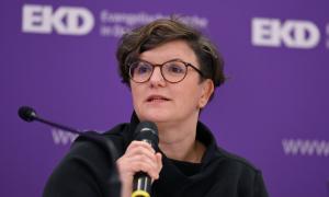 Eine Frau mit einem Mikrofon, hinter ihr der Schriftzug "EKD" auf lila Hintergrund
