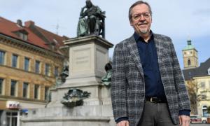 Älterer Mann steht vor einem Denkmal und Häusern im Hintergrund