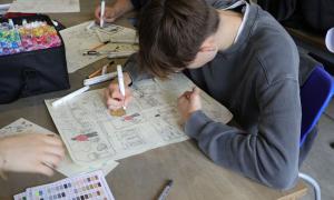 Ein Junge malt auf einem Blatt Papier und beugt sich dabei darüber