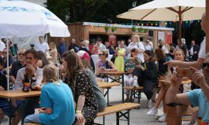 Menschen sitzen auf Bierbänken und unter Sonnenschirmen