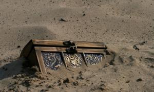 Eine Schatzkiste mit goldenen Beschlägen ragt aus Sand hervor
