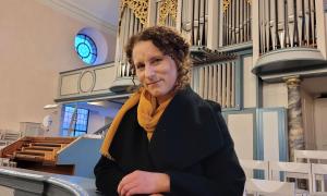 Frau mit braunen Haaren steht vor einer Orgel 