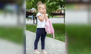 Ein Mädchen mit einem Rucksack schlägt die Hände vors Gesicht