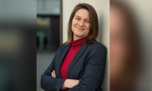 Frau mit braunen Haaren steht an einer Wand und lächelt