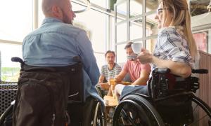 Menschen sitzen im Café, zwei von ihnen im Rollstuhl