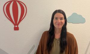 Eine Frau steht vor einer Wand, an der ein roter Heißluftballon und eine blaue Wolke angebracht sind