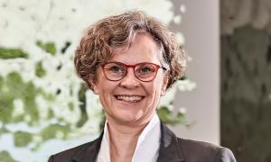 Eine Frau mit kurzen, lockigen Haaren und einer roten Brille lacht in die Kamera