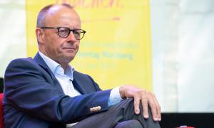 Ein Mann mit Brille im Anzug, er legt eine Hand auf sein Knie