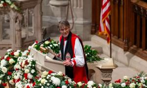 Eine Frau im Bischofsgewand steht auf einer Kanzel, hinter ihr die amerikanische Fahne, vor ihr Blumen