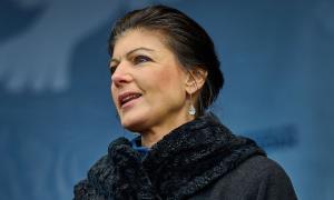 Eine Frau vor einer blauen Wand, sie trägt einen schwarzen Mantel mit auffälligem Kragen