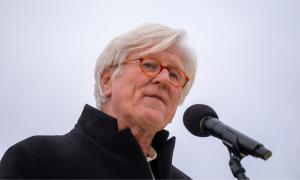 Ein Mann mit weißen Haaren und rötlicher Brille spricht in ein Mikrofon